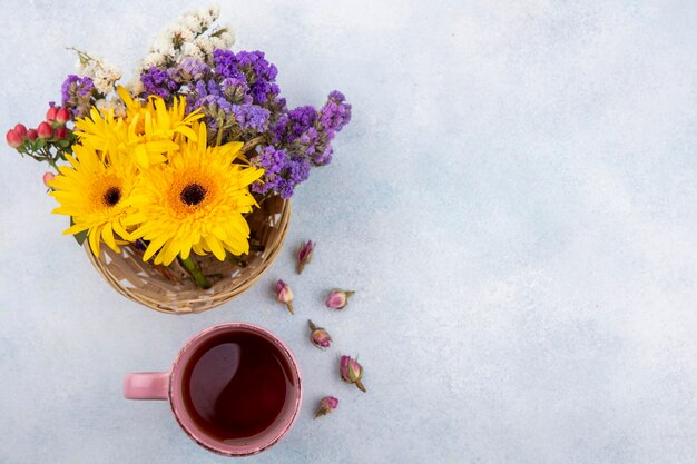 Draufsicht der Tasse Tee und der Blumen im Korb und auf Weiß mit Kopienraum