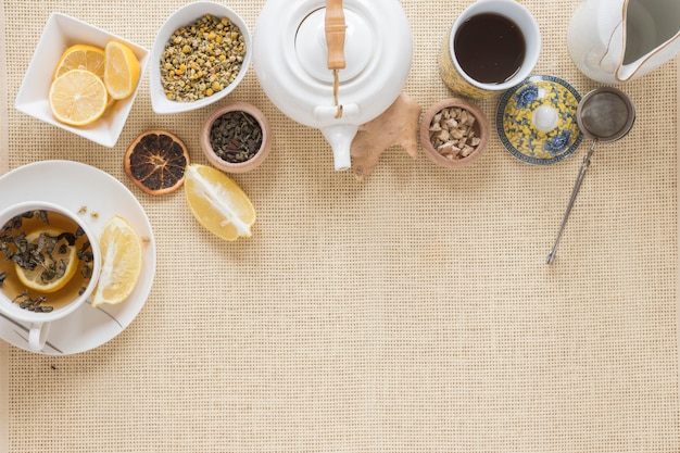 Draufsicht der Teekanne; Teesieb; Zitronenscheibe; trockene Grapefruit und getrocknete chinesische Chrysanthemenblüten auf Tischset