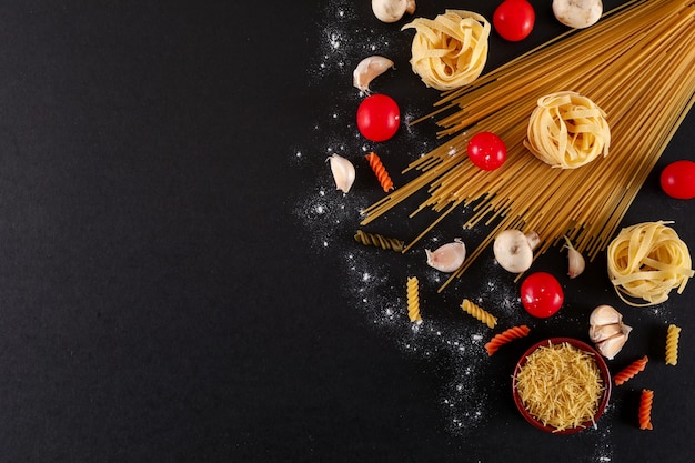 Draufsicht der Teigwarenkirschtomaten-Spaghettiteigwaren-Knoblauchs mit Kopienraum auf schwarzer Oberfläche