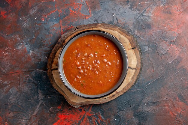 Draufsicht der Tomatensuppe in einer blauen Schüssel auf einem braunen Holztablett auf gemischter Farbtabelle