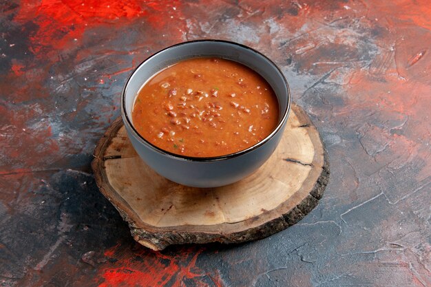 Draufsicht der Tomatensuppe in einer blauen Schüssel auf einem braunen Holztablett auf gemischter Farbtabelle