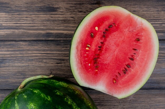 Draufsicht der Wassermelonenhälfte mit ganzem auf hölzernem Hintergrund