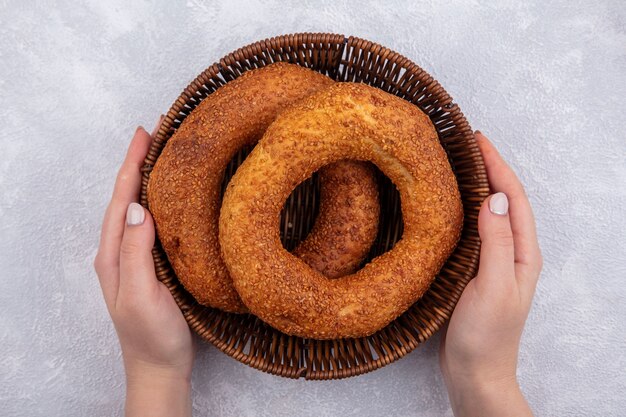 Draufsicht der weiblichen Hände, die einen Eimer mit traditionellem türkischem Bagel auf einem weißen Hintergrund halten