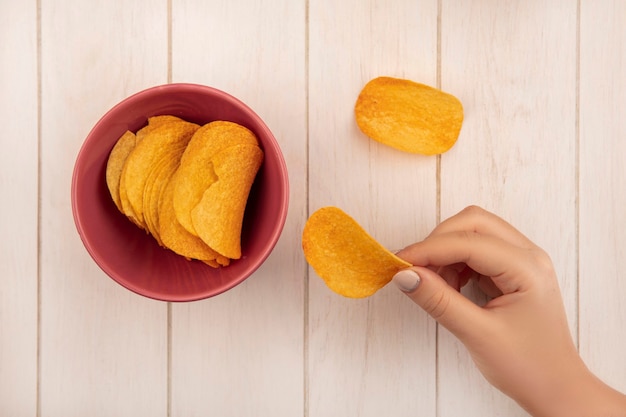 Draufsicht der weiblichen Hand, die leckere knusprige Chips auf einem beigen Holztisch hält