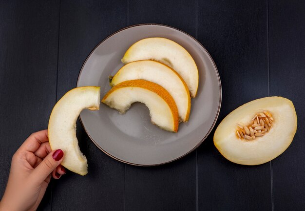 Draufsicht der weiblichen Hand, die Melonenscheibe mit Scheiben auf Platte auf Holz hält