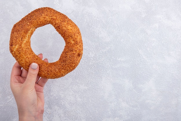 Draufsicht der weiblichen Hand, die türkischen Sesambagel auf einem weißen Hintergrund mit Kopienraum hält