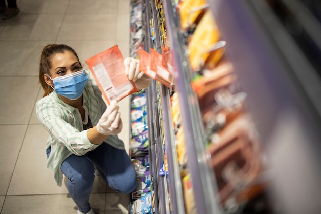 Draufsicht der weiblichen Person mit Maske und Handschuhen, die Lebensmittel im Supermarkt kaufen