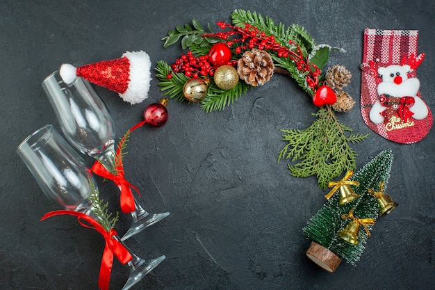 Draufsicht der Weihnachtsstimmung mit gefallenen Glasbechern-Tannenzweigen-Weihnachtsbaumsocken-Weihnachtsmann-Hut auf dunklem Hintergrund