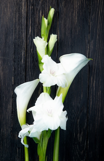 Kostenloses Foto draufsicht der weißen farbe gladiolen- und callalilienblumen lokalisiert auf schwarzem hintergrund