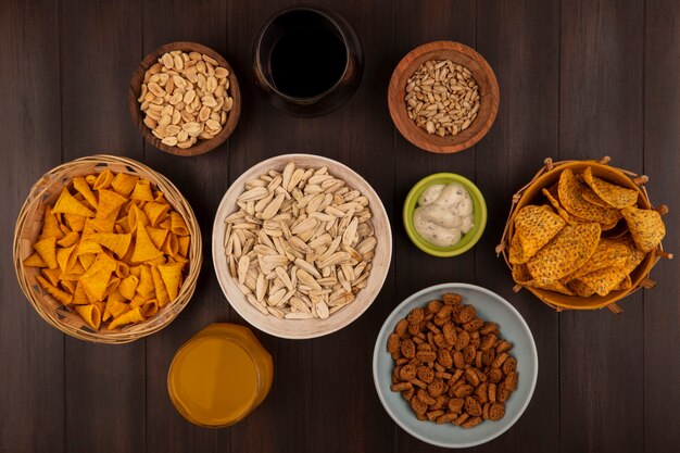 Draufsicht der weißen Sonnenblumenkerne auf einer Schüssel mit würzigen Chips auf einem Eimer mit Maissnacks auf einem Eimer mit Pinienkernen auf einer Holzschale mit Soße auf einer grünen Schüssel auf einem Holztisch