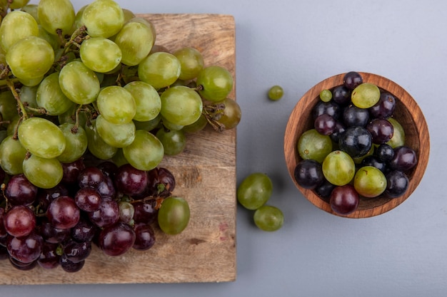 Draufsicht der weißen und roten Trauben auf Schneidebrett und Schüssel Traubenbeeren auf grauem Hintergrund