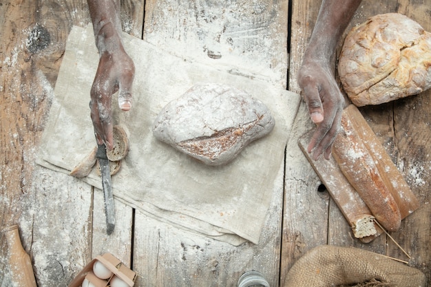 Draufsicht des afroamerikanischen Mannes kocht frisches Müsli, Brot, Kleie auf Holztisch