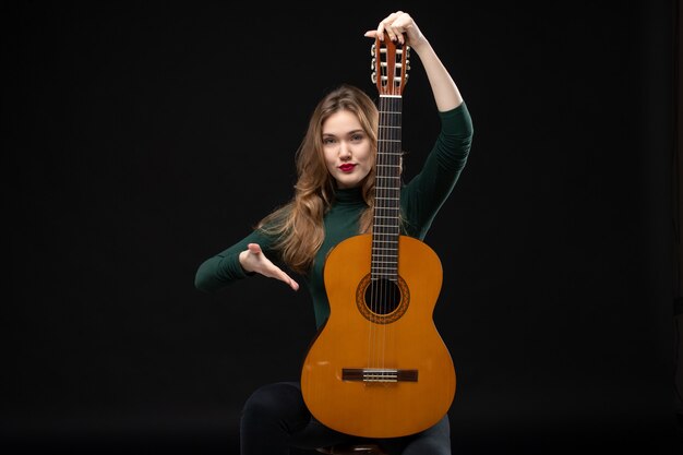 Draufsicht des blonden schönen Musikermädchens, das Gitarre hält und jemanden im Dunkeln begrüßt welcoming