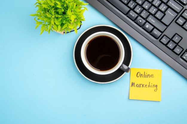 Draufsicht des Bürokonzepts mit einer Tasse schwarzem Tee und Online-Marketing-Schreibblume auf blauem Hintergrund