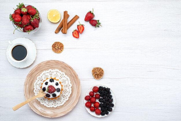 Draufsicht des cremigen Kuchens mit Beeren zusammen mit Zimtkaffeekirschen auf hellem Schreibtisch, Kuchen süß