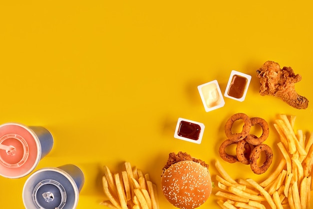 Draufsicht des Fast-Food-Gerichts. Fleischburger, Kartoffelchips und Wedges. Komposition mitnehmen. Pommes Frites, Hamburger, Mayonnaise und Ketchup-Saucen auf gelbem Hintergrund. Menü- oder Quittungshintergrund. Ansicht von oben.