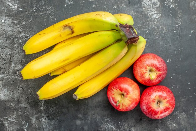 Draufsicht des frischen Bananenbündels der organischen Nahrungsquelle und der roten Äpfel auf dunklem Hintergrund