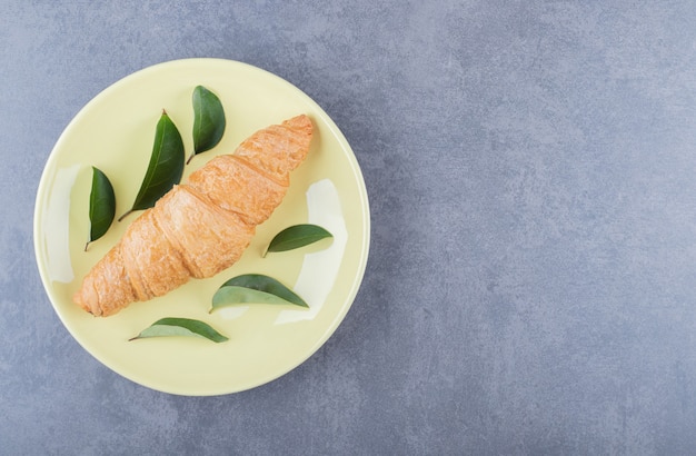 Draufsicht des frischen Croissants auf gelbem Teller mit Blättern.