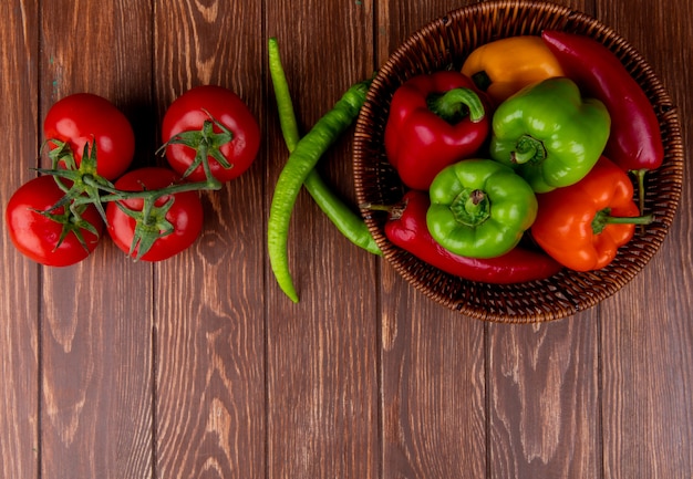 Draufsicht des frischen Gemüses bunte Paprikaschoten rote Chilischoten in einem Weidenkorb und frischen reifen Tomaten auf Holz rustikal