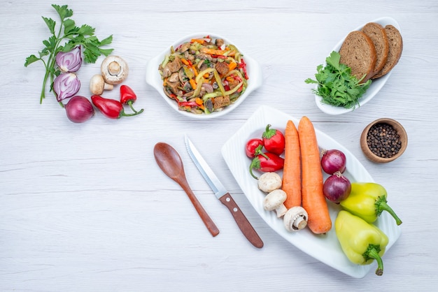 Draufsicht des frischen Gemüsesalats, der mit Fleisch zusammen mit Brotlaib und ganzem Gemüse und Gemüse auf hellem Schreibtisch, Gemüsesalat geschnitten wird