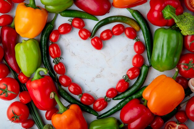 Draufsicht des frischen reifen Gemüses angeordnet in einer Herzform Kirschtomaten grüner Chili-Pfeffer-Paprika auf Marmorhintergrund