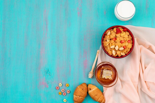 Draufsicht des Frühstücks mit Cornflakes, Früchten, Milch und Honig mit Kopienraum auf blauem Hintergrund horizontal