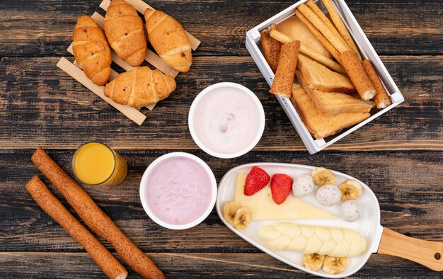 Draufsicht des Frühstücks mit Toast, Croissants, Joghurt und Käse auf dunkler Holzoberfläche horizontal