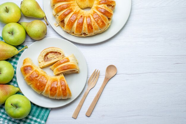 Draufsicht des gebackenen leckeren Gebäckarmreifs gebildet innerhalb der Glasplatte zusammen mit Äpfeln und Birnen auf weißem Schreibtisch, Gebäckkeks süßer Backkeks