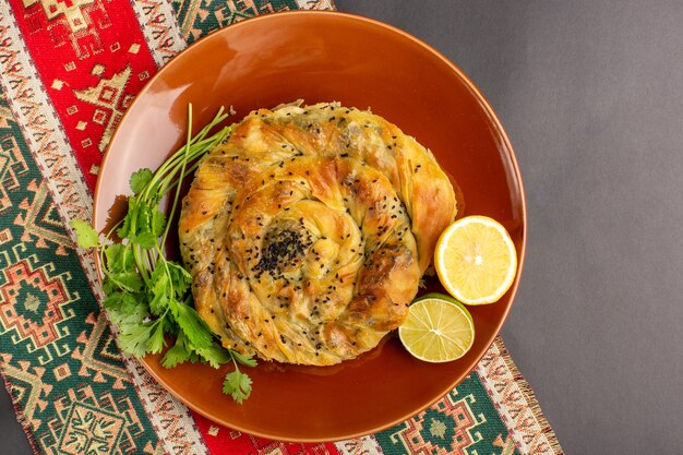 Draufsicht des Gebäcks mit Fleisch köstliche Teigmahlzeit innerhalb der braunen Platte mit Zitronenscheiben auf der dunklen Oberfläche