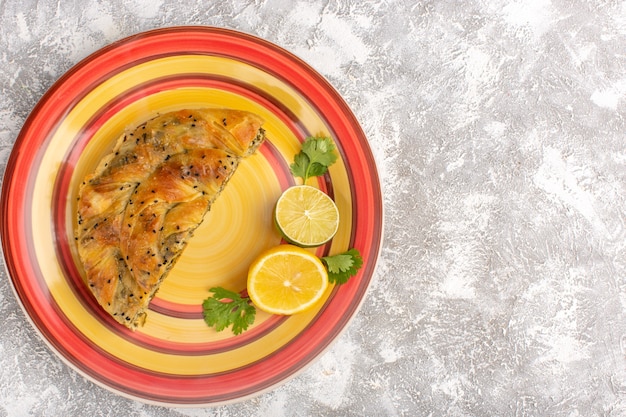 Draufsicht des Gebäcks mit Fleisch köstliche Teigmahlzeit innerhalb Platte geschnitten mit Zitrone auf hellweißer Oberfläche