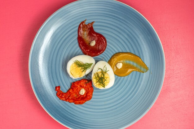 Draufsicht des gekochten Eies mit Ketchup und Senf innerhalb Platte auf rosa Wand