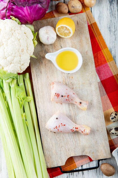 Draufsicht des Gemüses als Blumenkohl-Selleriekartoffel mit Butterhähnchenschenkeln Knoblauch und Zitrone auf Schneidebrett auf hölzernem Hintergrund