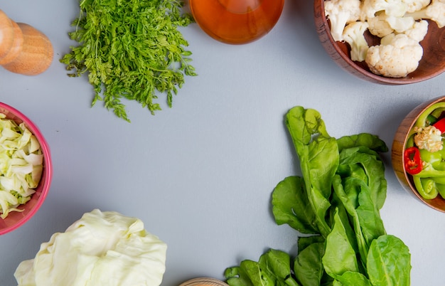 Draufsicht des Gemüses als ganzes und geschnittenes Kohlspinat-Bündel Koriander-Blumenkohl- und Pfefferscheiben mit geschmolzener Butter und Salz auf blauem Hintergrund