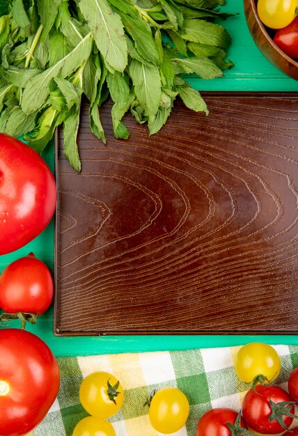 Draufsicht des Gemüses als grüne Minze hinterlässt Tomaten um leeres Tablett auf grüner Oberfläche