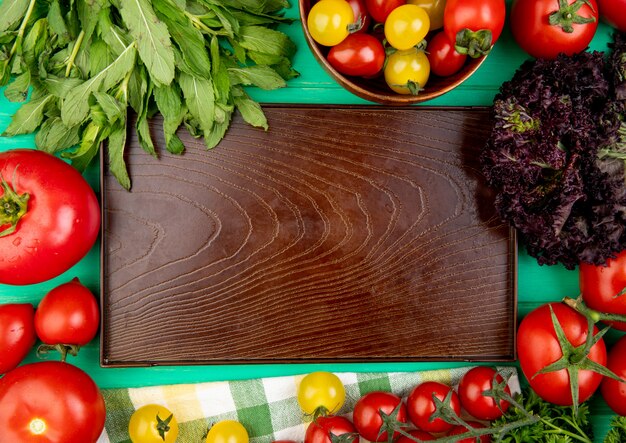 Draufsicht des Gemüses als grüne Minze verlässt Basilikum-Tomate um leeres Tablett auf grüner Oberfläche