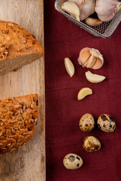 Draufsicht des Gemüses als Knoblauch und Ei mit halbem Schwarzbrotschnitt auf Holzoberfläche und burgunderfarbenem Hintergrund