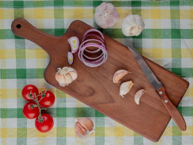 Draufsicht des Gemüses als Knoblauchzwiebeltomate mit Messer und Schneidebrett auf karierter Stoffoberfläche