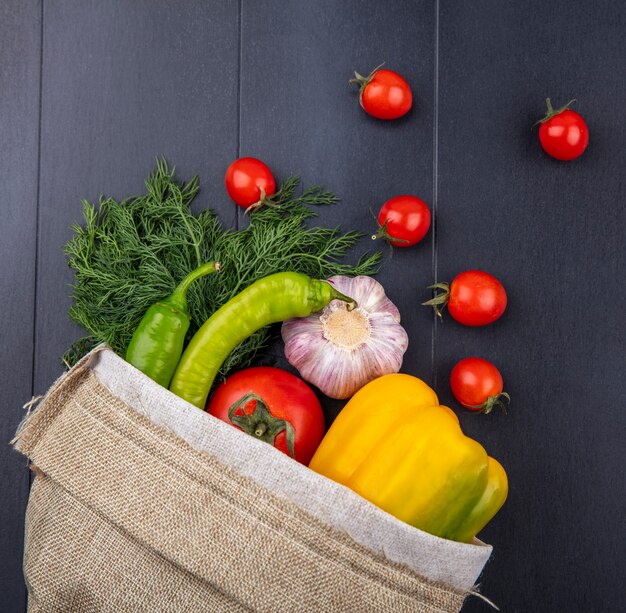 Draufsicht des Gemüses als Pfeffer-Tomaten-Knoblauch-Dill, der aus dem Sack auf schwarzer Oberfläche verschüttet wird