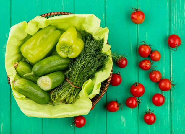 Draufsicht des Gemüses als Pfeffergurkendill im Korb mit Tomaten auf grüner Oberfläche