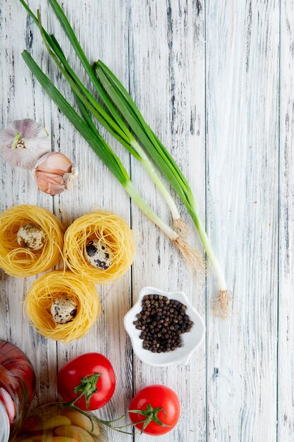 Draufsicht des Gemüses als Schalotten-Knoblauch-Tomaten-Ei mit schwarzem Pfeffer und Fadennudeln auf hölzernem Hintergrund mit Kopienraum