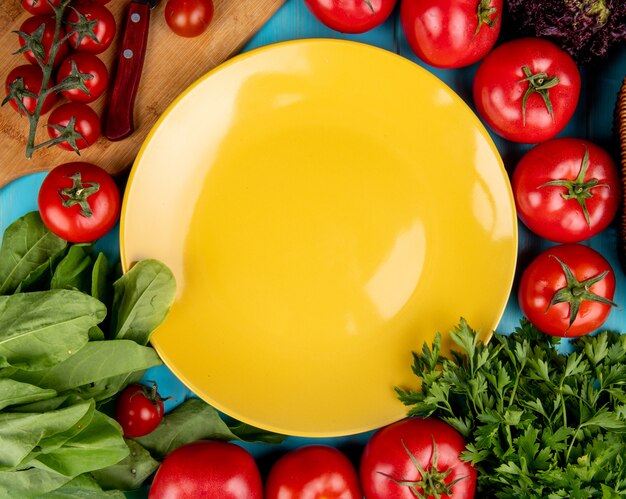 Draufsicht des Gemüses als Spinat-Basilikum-Tomatenkoriander mit Messer auf Schneidebrett und leerem Teller auf Blau