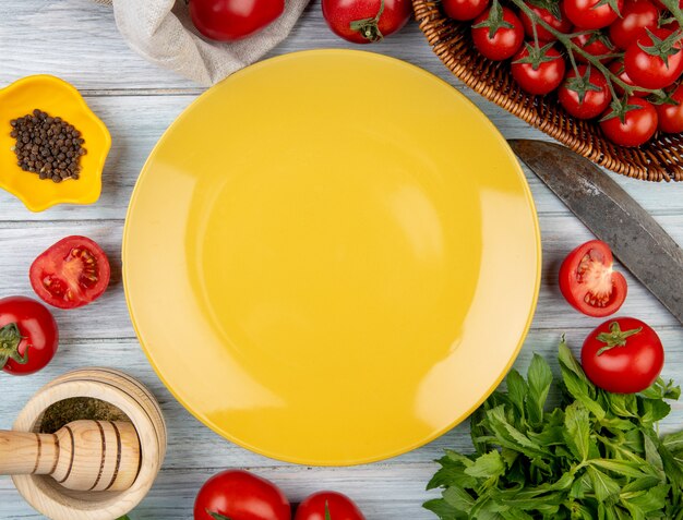 Draufsicht des Gemüses als tomatengrüne Minzblätter mit Knoblauchbrecher des schwarzen Pfeffers und Messer mit leerem Teller auf Holz