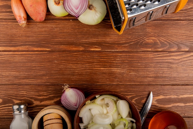Draufsicht des Gemüses als verschiedene Arten der ganzen geschnittenen und geschnittenen Zwiebelkartoffel mit Salzbuttermesser und Reibe auf hölzernem Hintergrund mit Kopienraum
