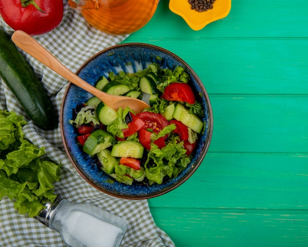 Draufsicht des Gemüsesalats mit Tomatensalat-Gurkensalz und schwarzem Pfeffer auf Stoff und Grün mit Kopienraum