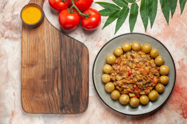 Draufsicht des gerösteten Auberginensalats auf Teller auf Schneidebrett-Tomaten auf nackter Oberfläche