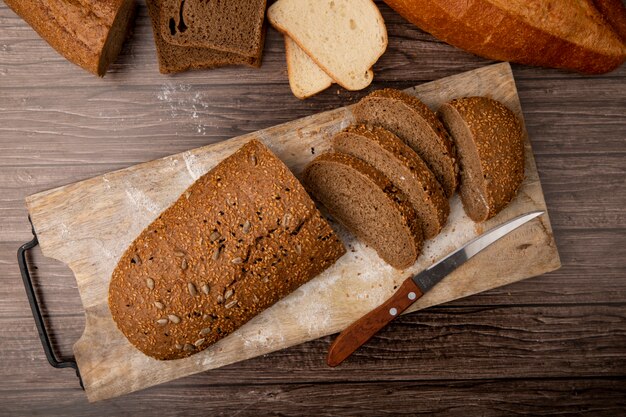 Draufsicht des geschnittenen und geschnittenen Sandwichbrotes und des Messers auf Schneidebrett auf hölzernem Hintergrund