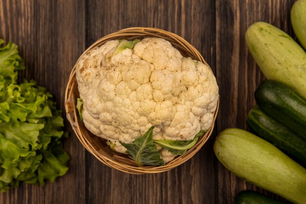 Draufsicht des gesunden Blumenkohls auf einem Eimer mit Gemüse wie Gurkensalat und Zucchini lokalisiert auf einer Holzwand