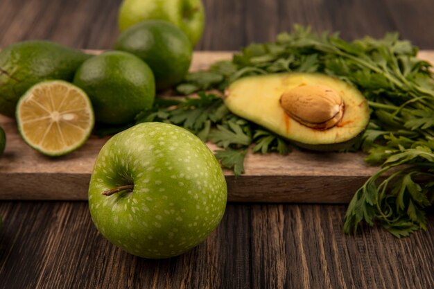 Draufsicht des gesunden grünen Apfels mit Limettenavocados und -petersilie lokalisiert auf einem hölzernen Küchenbrett auf einer Holzwand