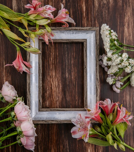 Draufsicht des grauen Rahmens mit Blumen um die Ränder auf einer Holzoberfläche