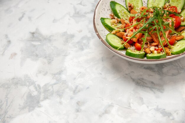 Draufsicht des hausgemachten gesunden köstlichen veganen Salats, der mit gehackten Gurken in einer Schüssel auf der linken Seite auf befleckter weißer Oberfläche verziert wird